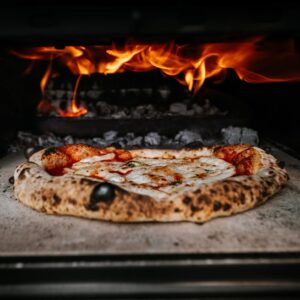 Close-up of authentic pizza cooking in a wood-fired oven with flames.