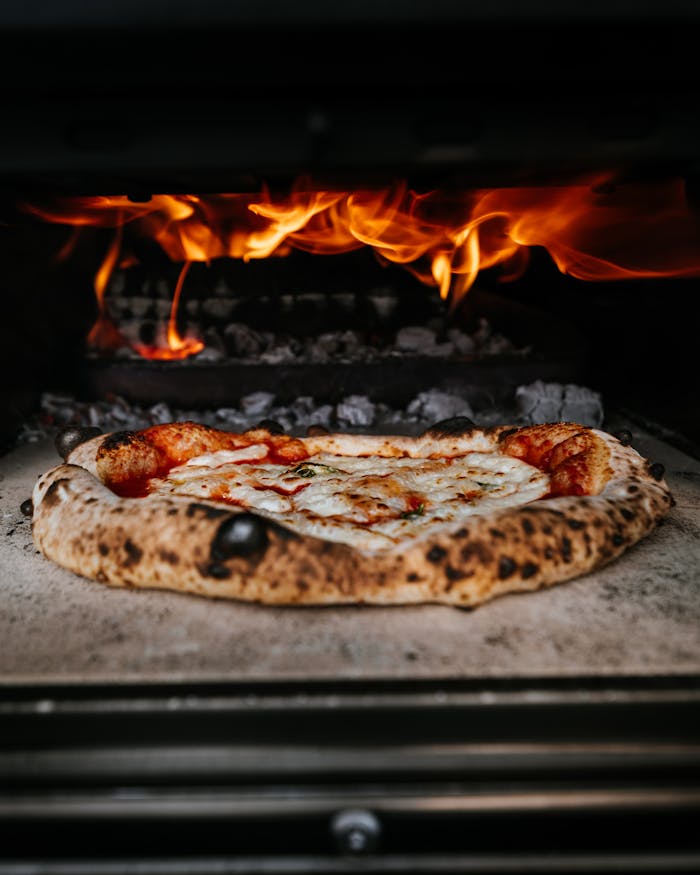 services-01 Close-up of authentic pizza cooking in a wood-fired oven with flames.