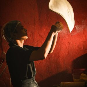 A chef skillfully tosses pizza dough in a warmly lit kitchen, showcasing traditional culinary artistry.